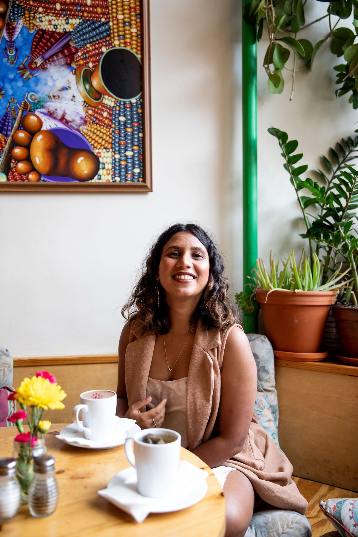 Tanisha smiling at a café table, folk art and plants around her
