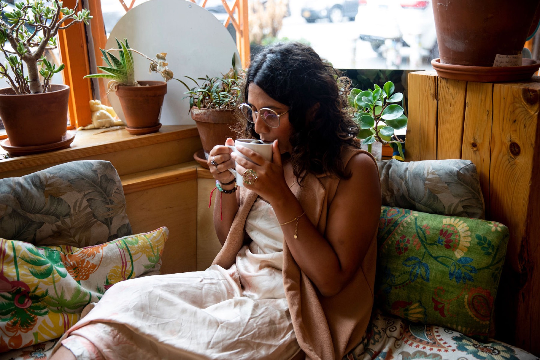 Tanisha on a couch with tea, mid-laugh, plants on the sill behind her