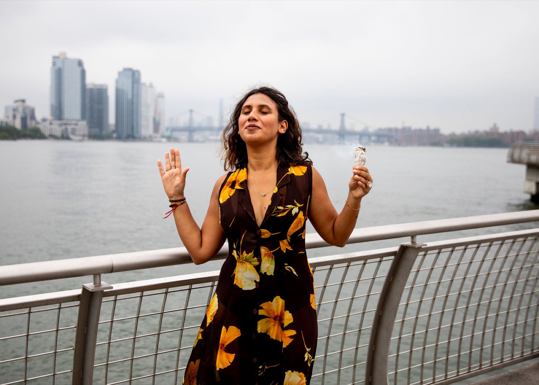 Tanisha dancing on a waterfront walkway, arms open, the city behind her
